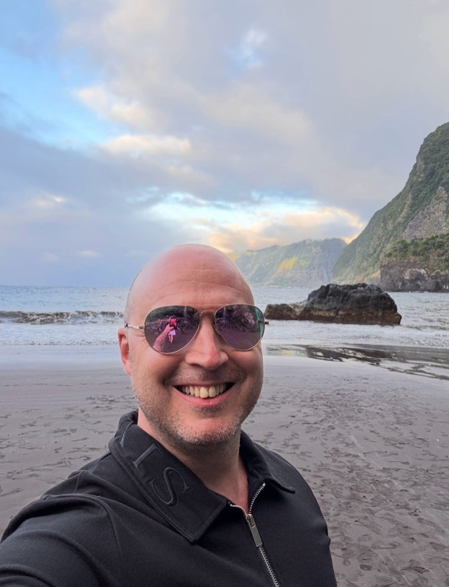 Craig smiling on a beach with cliffs in the background