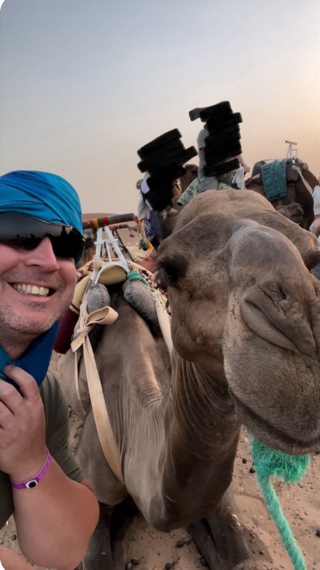 Craig smiling beside a camel while travelling