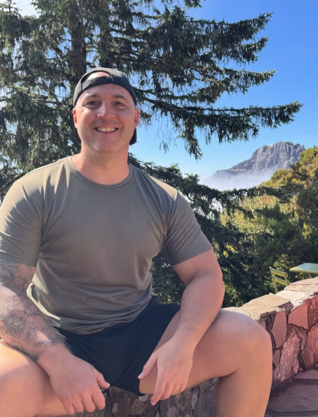 Craig smiling outdoors with mountains behind him